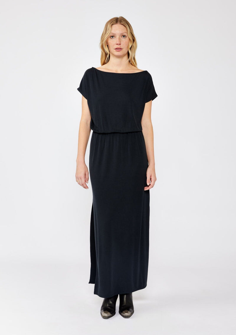 [Color: Black] A blonde model wearing a relaxed fit maxi that can be worn on or off shoulder. A casual black dress with a boat neckline, short dolman sleeves, elastic waistline, and side slits. Styled with black western boots for the fall season.