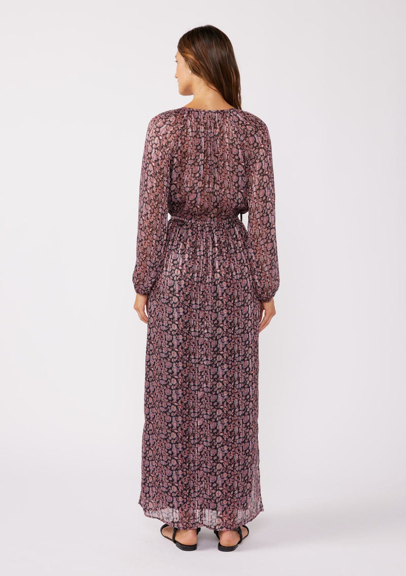 [Color: Black/Plum] A full body back image of a brunette model wearing a black and purple floral print maxi dress with shimmering metallic details. This holiday dress features long sleeves, a split v neckline with ties, an elastic waistline, and side slits. Perfect for festive gatherings and formal events. 