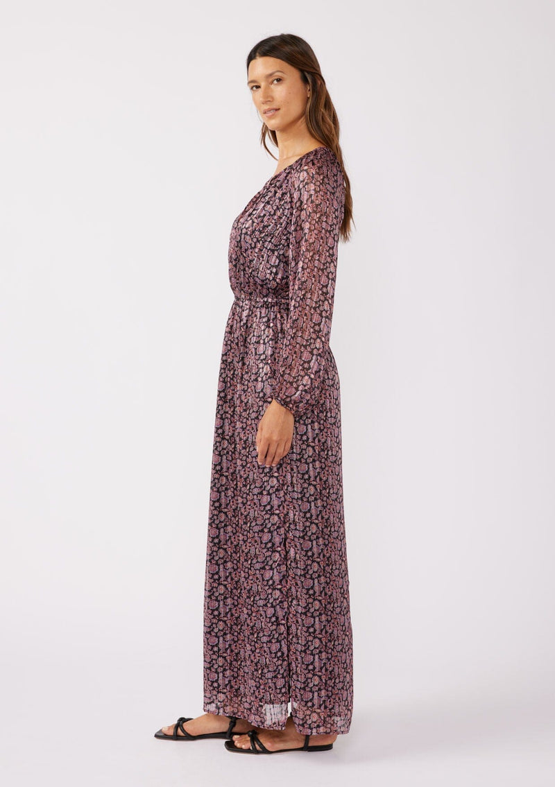 [Color: Black/Plum] A full body side image of a brunette model wearing a black and purple floral print maxi dress with shimmering metallic details. This holiday dress features long sleeves, a split v neckline with ties, an elastic waistline, and side slits. Perfect for festive gatherings and formal events. 