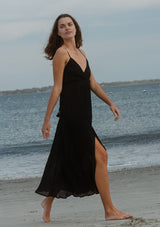 [Color: Black] A side image of a brunette model wearing a sleeveless, pleated maxi dress. This special occasion dress features a surplice v neckline, empire waistline, an adjustable strappy back, and a side slit. Perfect for the holidays or any special event. 