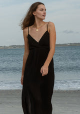 [Color: Black] A front image of a brunette model wearing a sleeveless, pleated maxi dress. This special occasion dress features a surplice v neckline, empire waistline, an adjustable strappy back, and a side slit. Perfect for the holidays or any special event. 