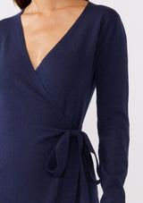 [Color: Navy] A brunette model wearing a sweater midi wrap dress in navy blue. Featuring a flattering v neckline, side tie closure, and long sleeves. A versatile cozy knit dress for the office or special occasions.  