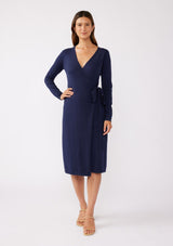 [Color: Navy] A brunette model wearing a sweater midi wrap dress in navy blue. Featuring a flattering v neckline, side tie closure, and long sleeves. A versatile cozy knit dress for the office or special occasions.  