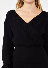 [Color: Black] A blonde wearing a cozy knit dress in black. A fitted sweater dress with a surplice v neckline, long sleeves, and a stretchy knit in cotton blend. Perfect for the fall season and colder temperatures.