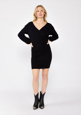 [Color: Black] A blonde wearing a cozy knit dress in black. A fitted sweater dress with a surplice v neckline, long sleeves, and a stretchy knit in cotton blend. Styled with black booties, perfect for the fall season and colder temperatures.