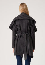 [Color: Charcoal] A blonde model wearing a dark grey pinstripe relaxed-fit, mid-length belted coat with an oversized shawl collar and side pockets. 