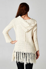 [Color: Natural] A brunette model wearing an off white vintage bohemian knit fringed sweater with a tie string hood and a long hemline. 