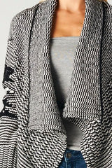 [Color: Ivory/Black] A detailed image of a beautiful chunky black and ivory knit cardigan with a shawl collar and ribbed detail. A western fall style cardigan with a cascading open front, long sleeves, and cozy side pockets. 