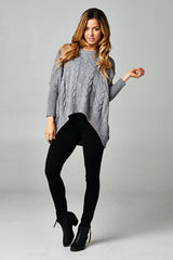 [Color: Grey/Black] A blonde model wearing a grey speckled cable knit pullover sweater with long dolman sleeves, a crew neckline, and a high low hemline. 