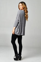 [Color: Grey/Black] A blonde model wearing a grey speckled cable knit pullover sweater with long dolman sleeves, a crew neckline, and a high low hemline. 