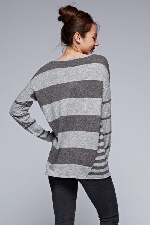 [Color: Charcoal/Heather Grey] A back facing image of a brunette model wearing a grey patchwork striped knit pullover with a v-neckline, long sleeves, dropped shoulders, and exposed seams. 