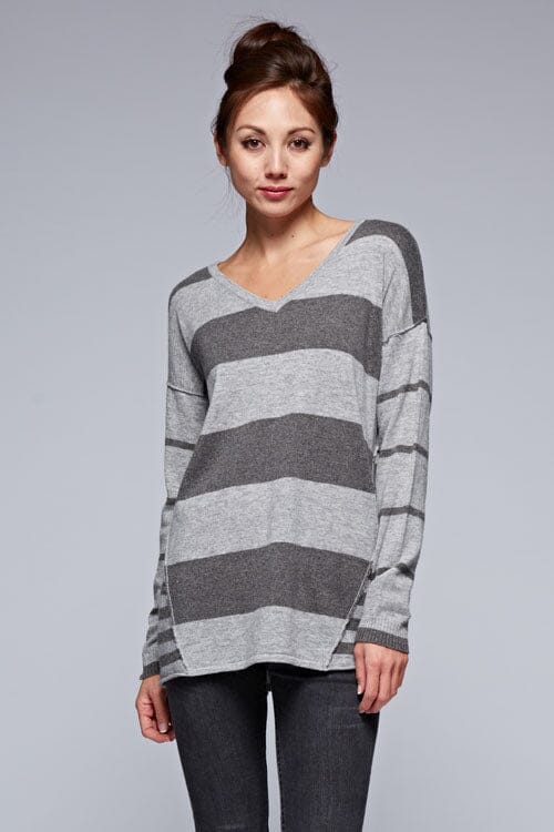 [Color: Charcoal/Heather Grey] A front facing image of a brunette model wearing a grey patchwork striped knit pullover with a v-neckline, long sleeves, dropped shoulders, and exposed seams. 