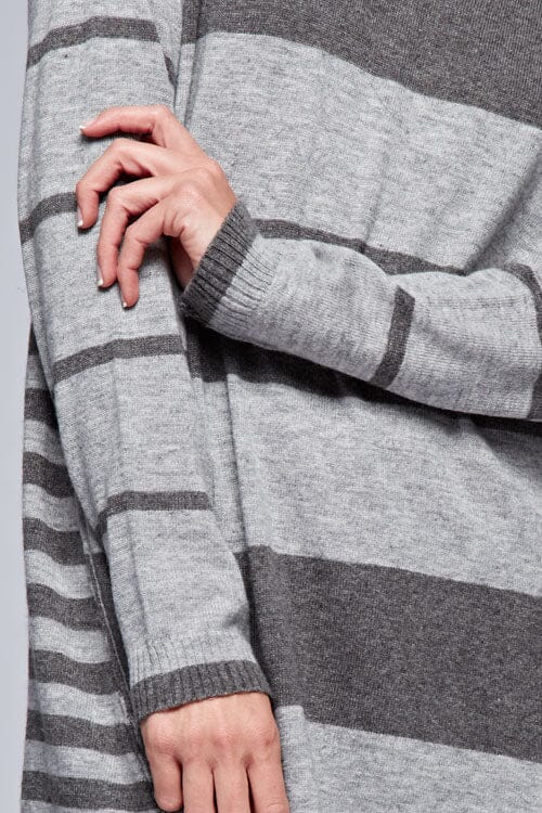 [Color: Charcoal/Heather Grey] A detail image of a brunette model wearing a grey patchwork striped knit pullover with a v-neckline, long sleeves, dropped shoulders, and exposed seams. 