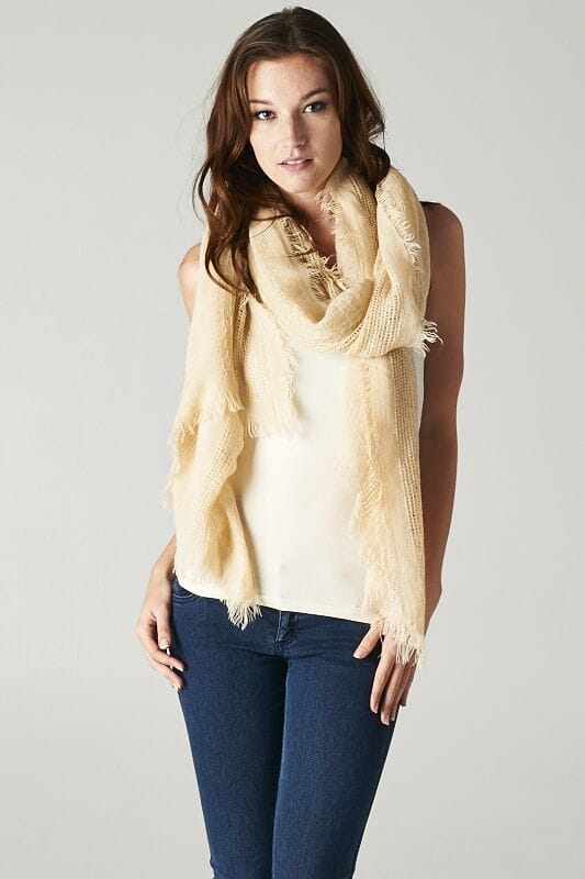 [Color: Beige] A brunette model wearing a beige, lightweight textured scarf with delicate fringed trim, styled as a cozy accessory to elevate a casual look.