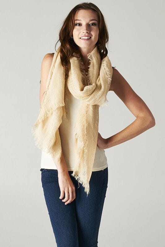 [Color: Beige] A brunette model wearing a beige, lightweight textured scarf with delicate fringed trim, styled as a cozy accessory to elevate a casual look.