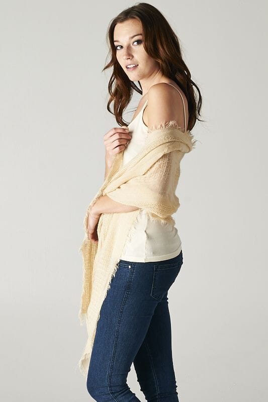 [Color: Beige] A brunette model wearing a beige, lightweight textured scarf with delicate fringed trim, styled as a cozy accessory to elevate a casual look.