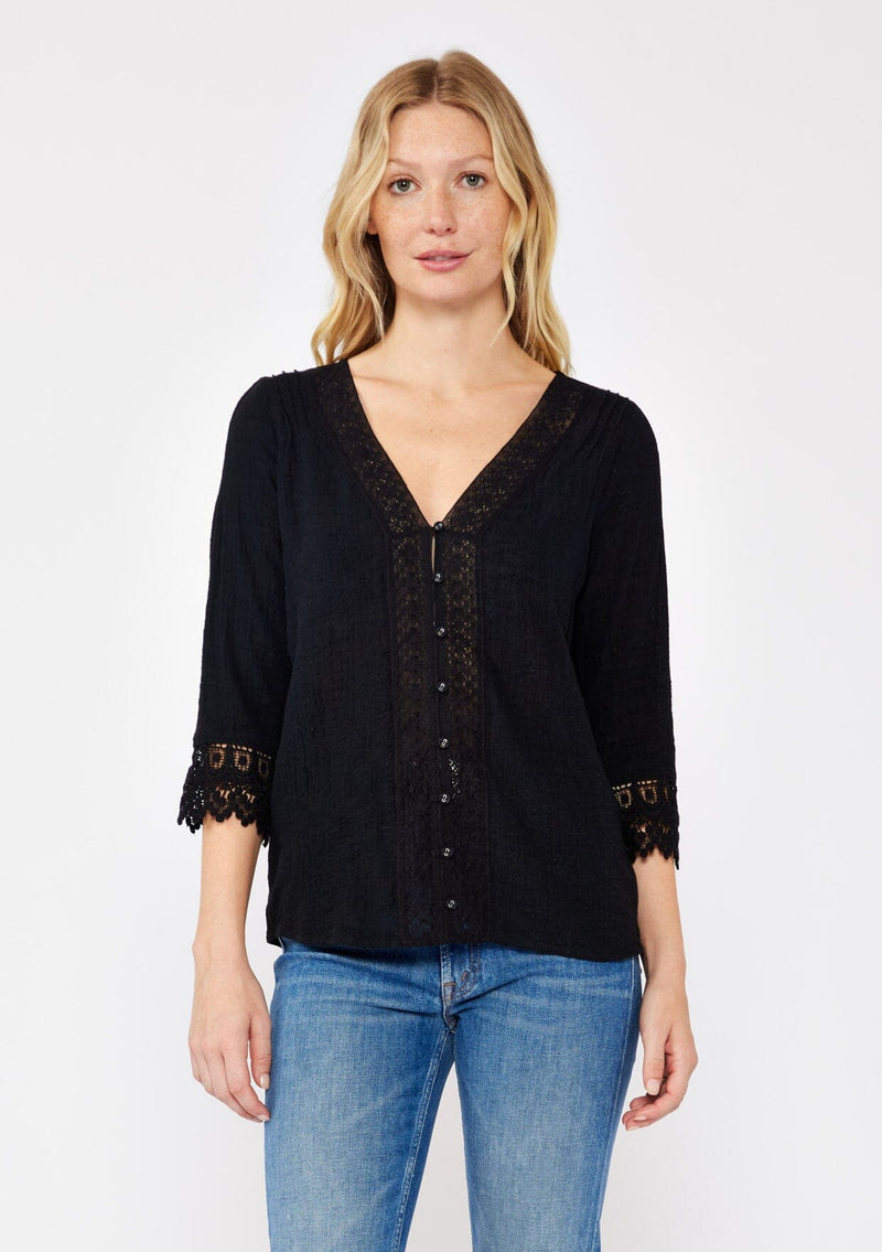 [Color: Black] A blonde model wearing a textured cotton blouse in black. With lace and crochet trims, functional button front, v neckline, and relaxed fit. A casual bohemian top paired with denim jeans. 