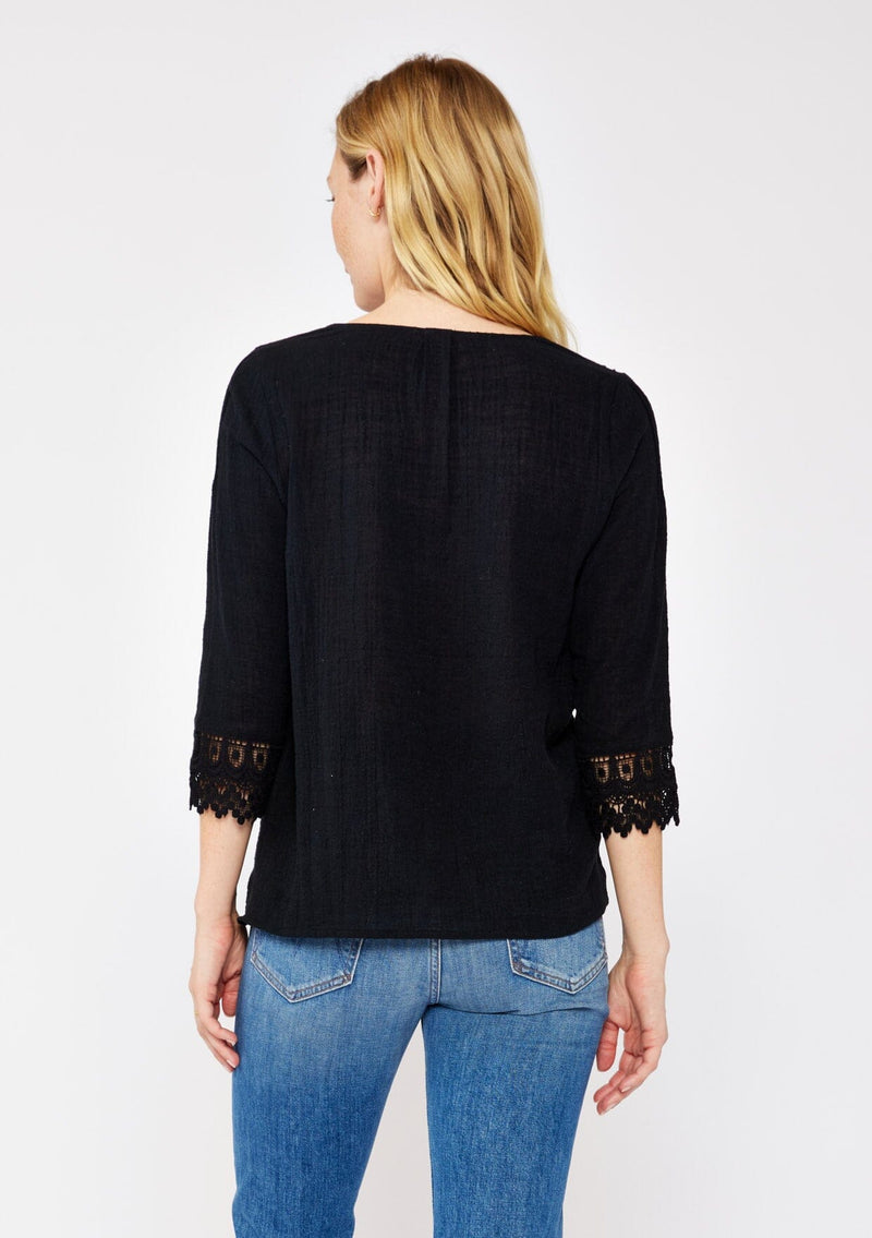 [Color: Black] A blonde model wearing a textured cotton blouse in black. With lace and crochet trims, functional button front, v neckline, and relaxed fit. A casual bohemian top paired with denim jeans.