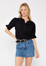 [Color: Black] A front facing image of a blonde model wearing a black bohemian cotton blend blouse in a textured gingham. With short puff sleeves, a button front, a high ruffled neckline, and smocked elastic details at the sleeve.