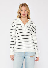 [Color: White/Black] A blonde model wearing a cozy knit  stripe pullover sweater in black and white. With a zip-up funnel neck with v neckline, long sleeve, and ribbed hem and sleeves. A relaxed fit sweater styled with distressed denim jeans for an ultra boho fall look. 