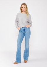 [Color: Heather Grey] A blonde model wearing a grey relaxed fit sweater with an asymmetrical neckline and long sleeves with a dropped shoulder. An everyday pullover sweater styled with denim jeans for the fall season.