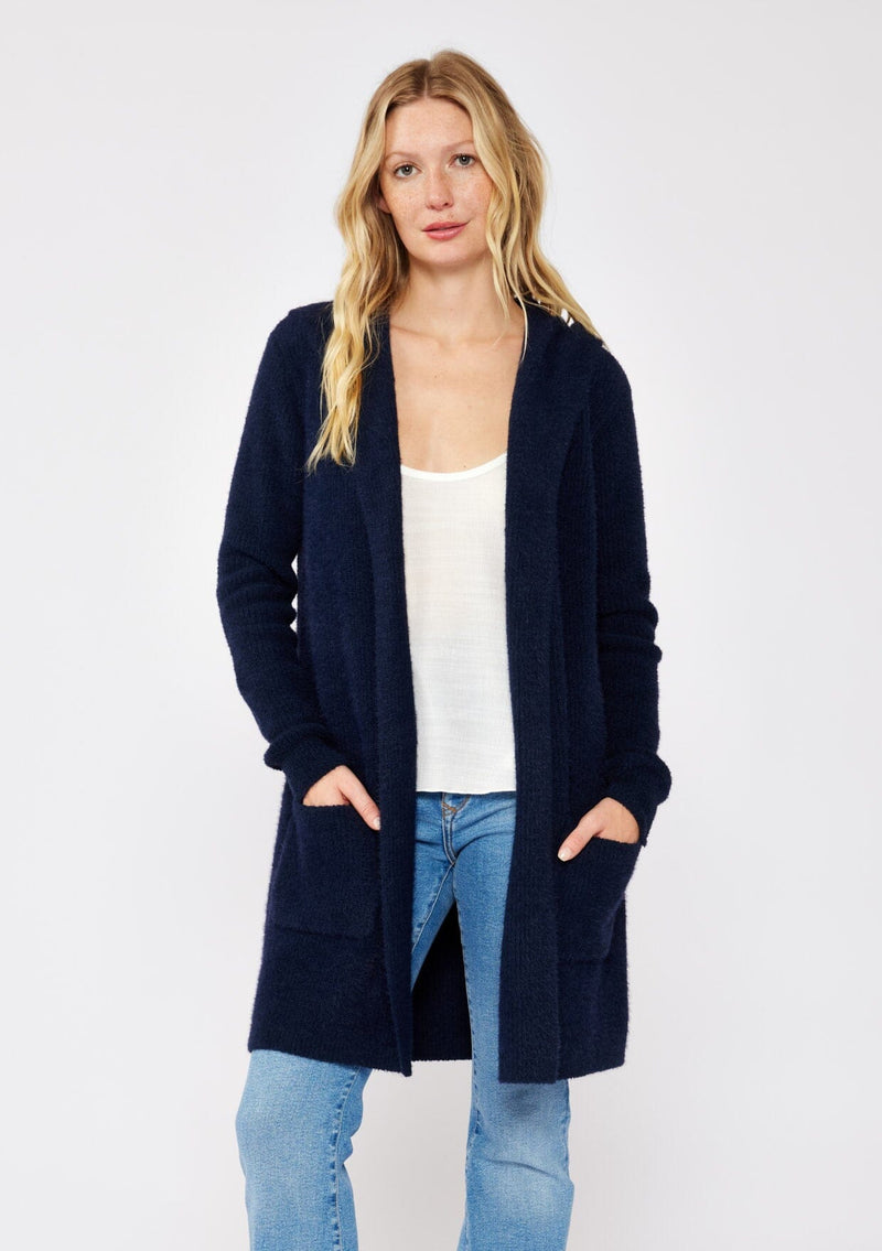 [Color: Navy] A navy blue cardigan with a fuzzy texture and soft touch. Features a hood, long sleeves, and patch pockets. A versatile cardigan layered with a white top for easy styling. Paired and styled with vintage denim and boots for the ultimate cozy look.