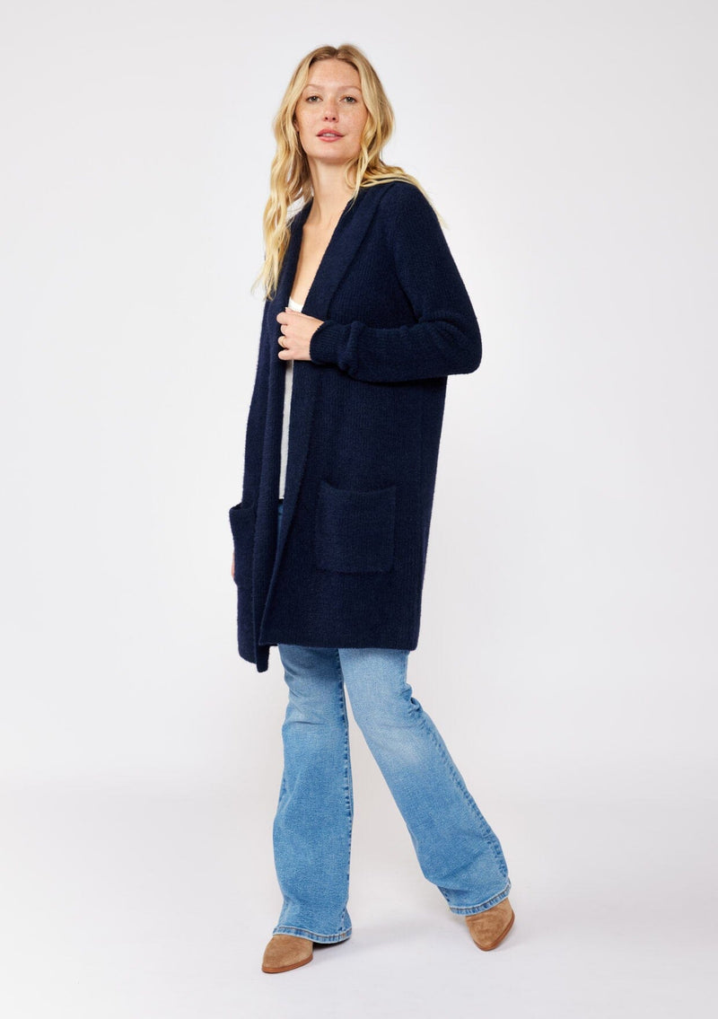 [Color: Navy] A navy blue cardigan with a fuzzy texture and soft touch. Features a hood, long sleeves, and patch pockets. A versatile cardigan layered with a white top for easy styling. Paired and styled with vintage denim and boots for the ultimate cozy look. 