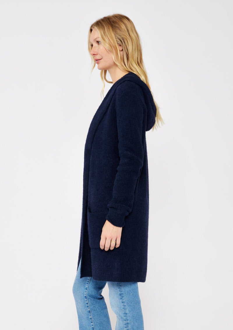 [Color: Navy] A navy blue cardigan with a fuzzy texture and soft touch. Features a hood, long sleeves, and patch pockets. A versatile cardigan layered with a white top for easy styling. Paired and styled with vintage denim and boots for the ultimate cozy look.