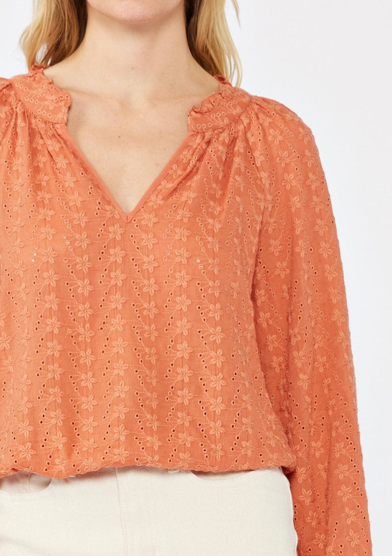 [Color: Terracota] A blonde model wearing a pretty floral embroidered top with eyelet details. A breezy Fall top with a ruffled split v neckline and long sleeves with an elastic cuff. An everyday burnt orange styled with casual light beige pants.