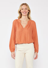 [Color: Terracota] A blonde model wearing a pretty floral embroidered top with eyelet details. A breezy Fall top with a ruffled split v neckline and long sleeves with an elastic cuff. An everyday burnt orange styled with casual light beige pants. 