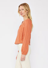 [Color: Terracota] A blonde model wearing a pretty floral embroidered top with eyelet details. A breezy Fall top with a ruffled split v neckline and long sleeves with an elastic cuff. An everyday burnt orange styled with casual light beige pants.