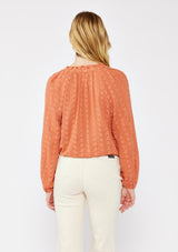 [Color: Terracota] A blonde model wearing a pretty floral embroidered top with eyelet details. A breezy Fall top with a ruffled split v neckline and long sleeves with an elastic cuff. An everyday burnt orange styled with casual light beige pants.