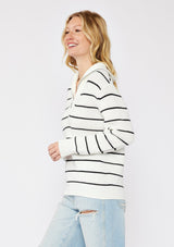 [Color: White/Black] A blonde model wearing a cozy knit stripe pullover sweater in black and white. With a zip-up funnel neck with v neckline, long sleeve, and ribbed hem and sleeves. A relaxed fit sweater styled with distressed denim jeans for an ultra boho fall look.