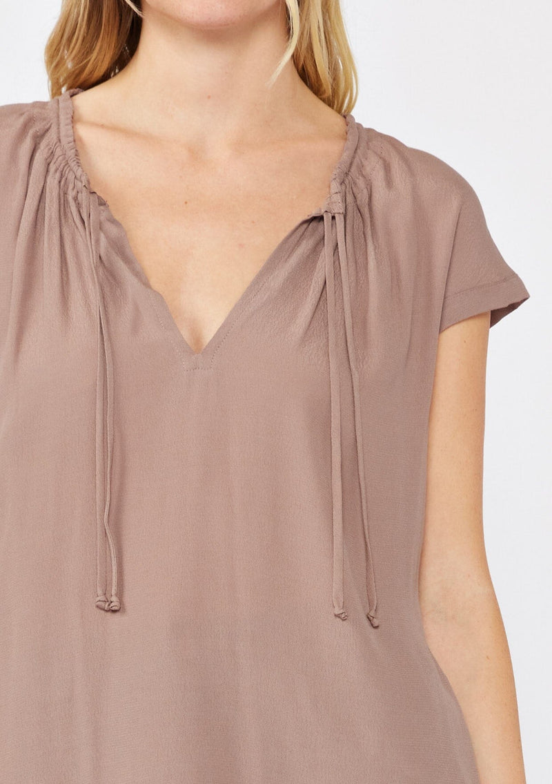 [Color: Mocha] A detailed image of a blonde model wearing a relaxed fit brown mocha top. With self neck ties, ruched split v neckline, and short dolman sleeves. 