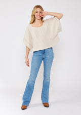 [Color: Natural] A blonde model wearing a soft cotton gauze top in beige natural. With a scoop neckline, embroidered front detail, and kimono sleeves. A relaxed fit top for lounging or a casual day out. Paired with denim jeans and boots for a laid back Fall season style.