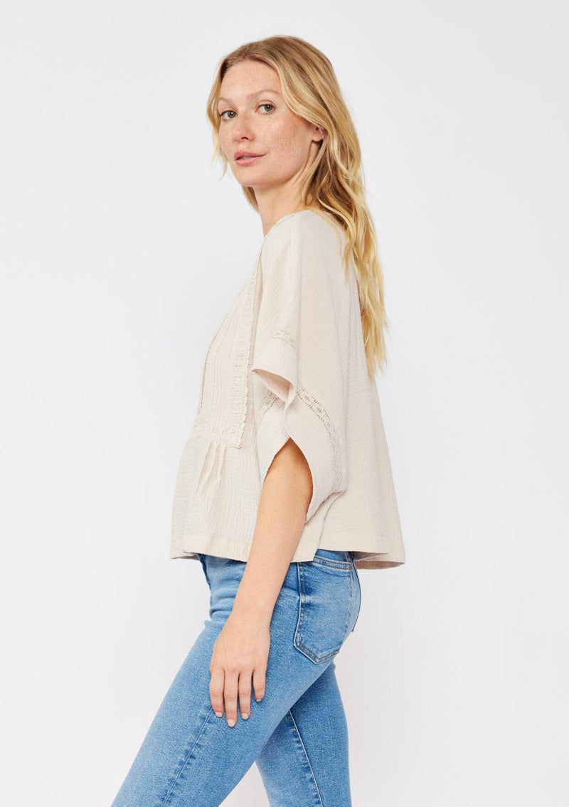 [Color: Natural] A blonde model wearing a soft cotton gauze top in beige natural. With a scoop neckline, embroidered front detail, and kimono sleeves. A relaxed fit top for lounging or a casual day out. Paired with denim jeans for a laid back style.