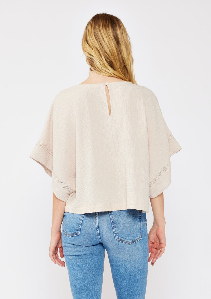 [Color: Natural] A blonde model wearing a soft cotton gauze top in beige natural. With a scoop neckline, embroidered front detail, and kimono sleeves. A relaxed fit top for lounging or a casual day out. Paired with denim jeans for a laid back style.