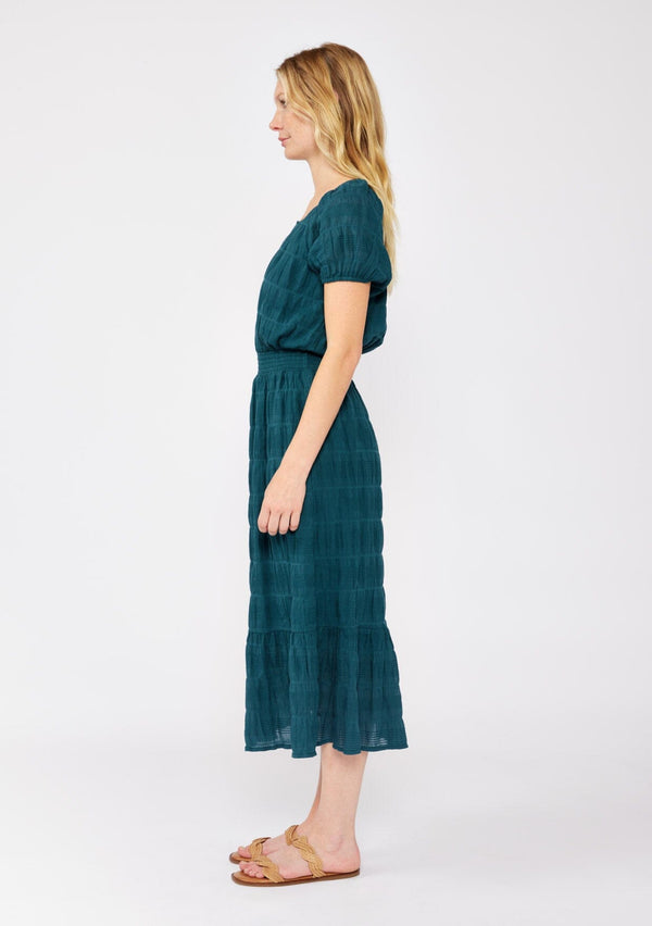 [Color: Deep Teal] A blonde model wearing a teal midi dress with a subtle woven striped design. With a split v-neckline, short puff sleeves, smocked waistline, and a ruffle trimmed hem.