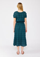 [Color: Deep Teal] A blonde model wearing a teal midi dress with a subtle woven striped design. With a split v-neckline, short puff sleeves, smocked waistline, and a ruffle trimmed hem.