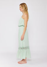 [Color: Dusty Sage] A blonde model wearing a minty green ultra bohemian maxi dress for vacation. This summer maxi dress features a halter neckline and a comfortable smocked waist. This dress is also embellished with intricate lace details and embroidered eyelet. The perfect style for brunch or a tropical vacation.