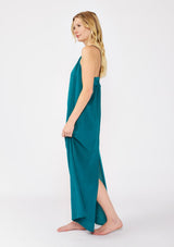 [Color: Forest Teal] A blonde model wearing a flowy, casual summer dress in a teal solid print. With a v neckline, relaxed fit, and faux braided leather straps that are adjustable at the back. A cute back slit dress for the summer season, perfect for vacation or beachside stroll. Classic cotton dress.