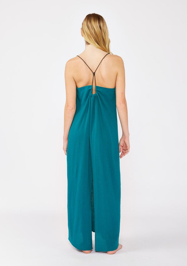 [Color: Forest Teal] A blonde model wearing a flowy, casual summer dress in a teal solid print. With a v neckline, relaxed fit, and faux braided leather straps that are adjustable at the back. A cute back slit dress for the summer season, perfect for vacation or beachside stroll. Classic cotton dress.