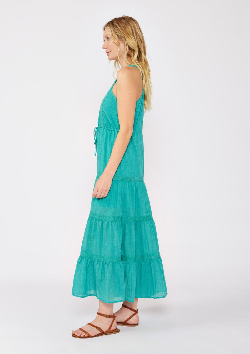 [Color: Teal] A blonde model wearing a Victorian vintage inspired bohemian maxi dress in the color teal. With a v neckline, button front, and delicate lace trims. A summer tank maxi dress with a flowy relaxed fit paired with brown strappy sandals for warm weather.