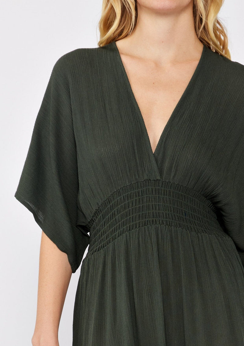 [Color: Military] An image of a blonde model wearing a classic casual military maxi dress. With half-length kimono sleeves, a plunging v neckline, a smocked elastic empire waist, side slits, and an open back with tie closure.