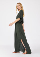 [Color: Military] An image of a blonde model wearing a classic casual military maxi dress. With half-length kimono sleeves, a plunging v neckline, a smocked elastic empire waist, side slits, and an open back with tie closure.