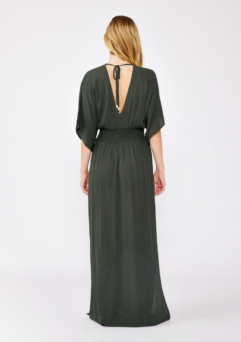 [Color: Military] An image of a blonde model wearing a classic casual military maxi dress. With half-length kimono sleeves, a plunging v neckline, a smocked elastic empire waist, side slits, and an open back with tie closure.