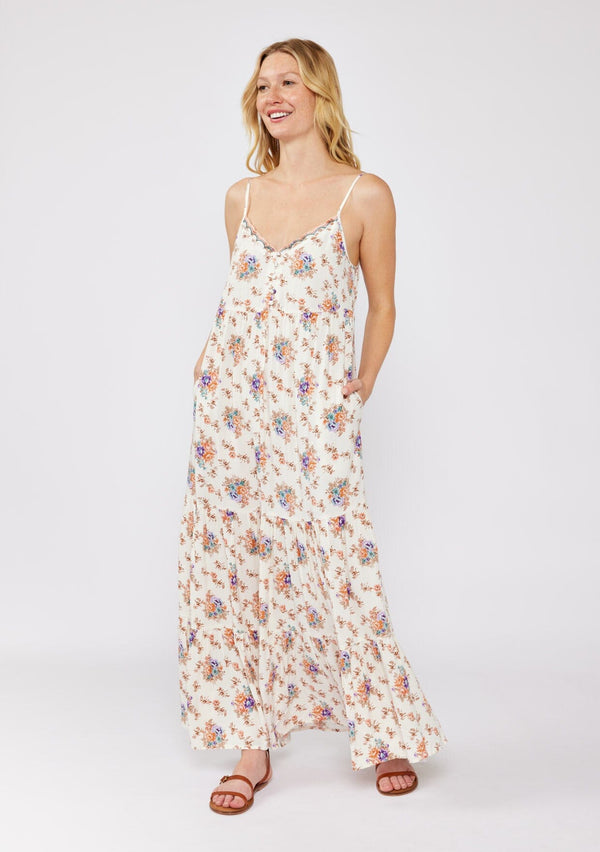 [Color: Natural/Rust] A blonde model wearing a flowy ultra bohemian maxi dress in a vintage ivory and dusty pink floral print. A relaxed fit dress with a tiered skirt, side pockets, scalloped v neckline, and adjustable spaghetti strap. A very breezy dress styled with bohemian strappy flats for a laid back look.