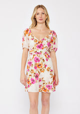 [Color: Natural/Orchid] A blonde model wearing a pretty floral mini dress in pink and orange. With a surplice v neckline, puff sleeves, attached waist belt with multiple styling opportunities, and smocked back. A floral fall dress for special occasions and  dinner parties. 