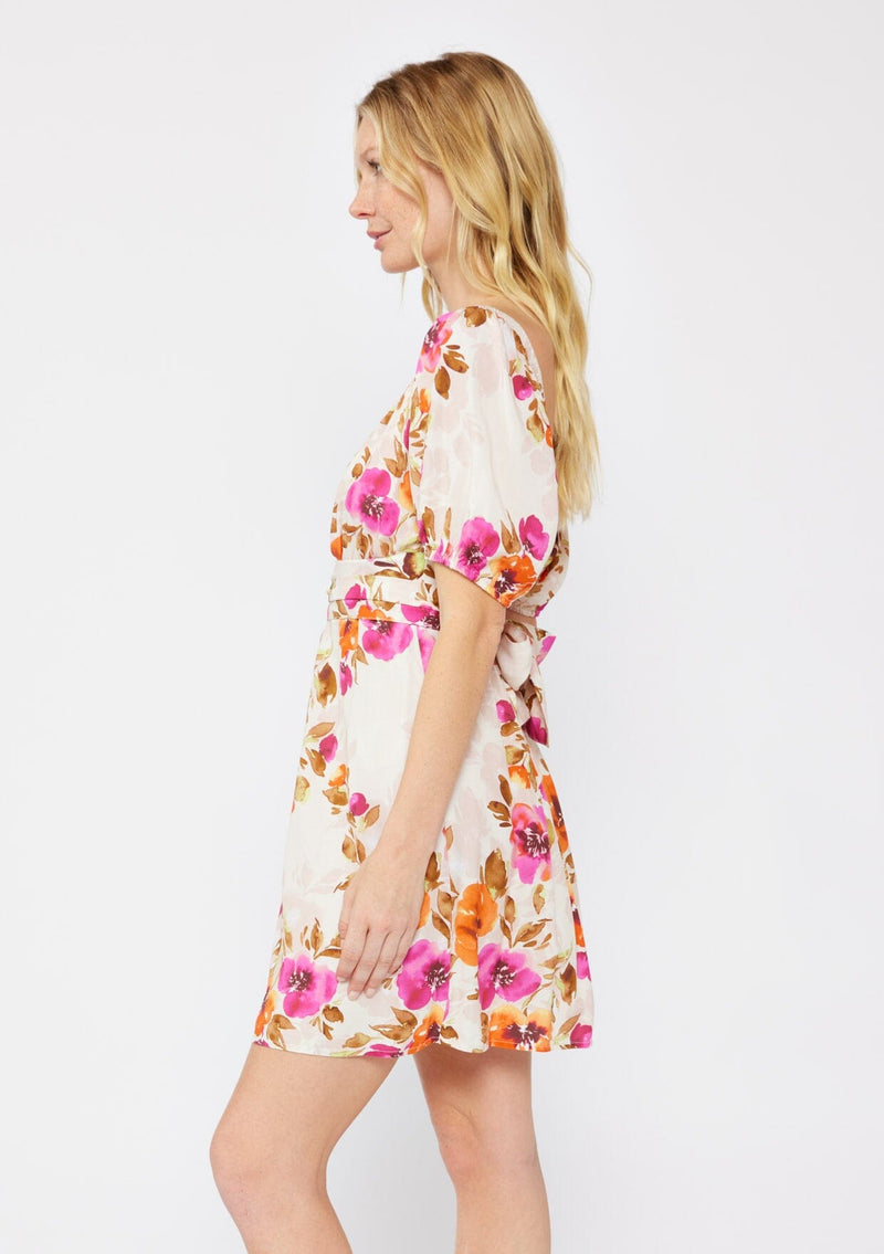 [Color: Natural/Orchid] A blonde model wearing a pretty floral mini dress in pink and orange. With a surplice v neckline, puff sleeves, attached waist belt with multiple styling opportunities, and smocked back. A floral fall dress for special occasions and dinner parties.