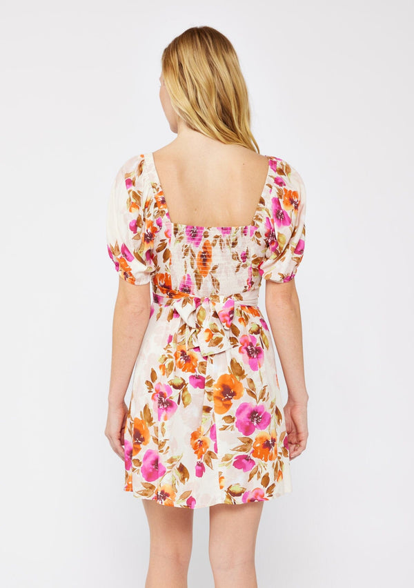 [Color: Natural/Orchid] A blonde model wearing a pretty floral mini dress in pink and orange. With a surplice v neckline, puff sleeves, attached waist belt with multiple styling opportunities, and smocked back. A floral fall dress for special occasions and dinner parties.